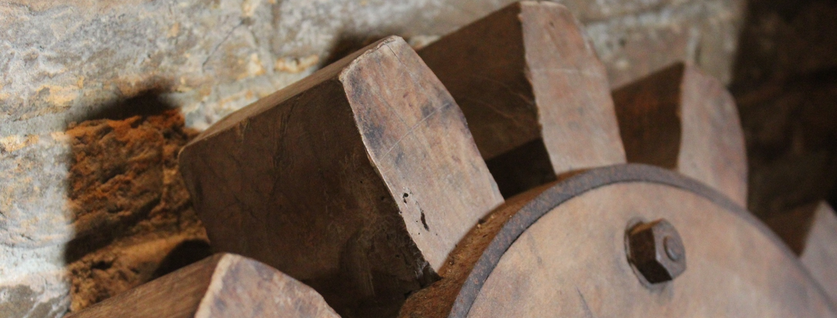 Picture of a wooden gear leaning against a stone wall