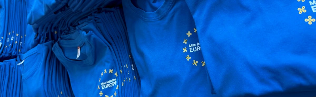 Photo of a pile of blue t-shirts with the Mac Admins Europe logo, a circle of 12 gold symbols around words Mac Admins Europe in white
