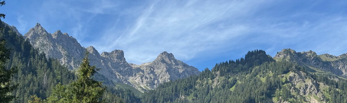 Image of a mountain range behind some ridges with green forest and a blue summer sky